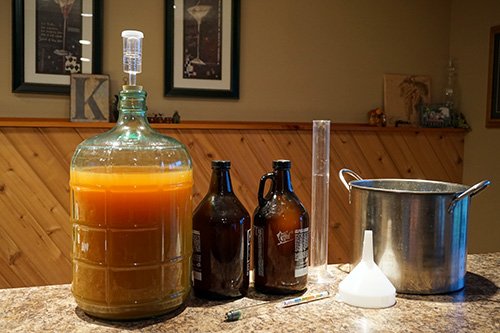a carboy full of cider next to two growlers and a brew kettle