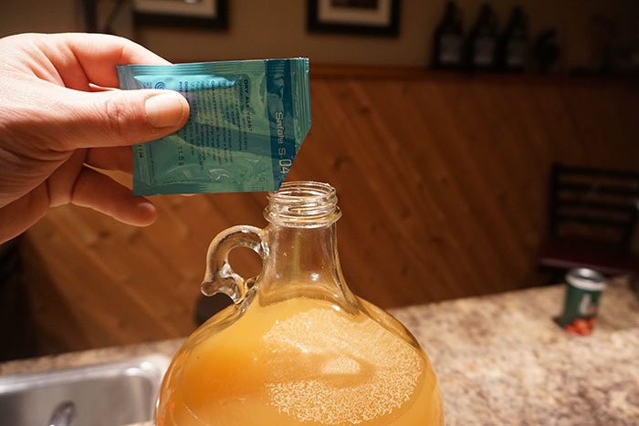a hand pouring a pack of yeast into a carboy of apple cider