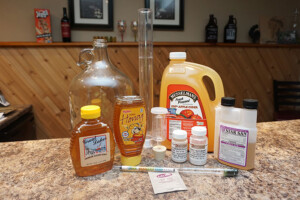 a collection of ingredients for an apple cyser including cider, honey, yeast, and yeast nutirent