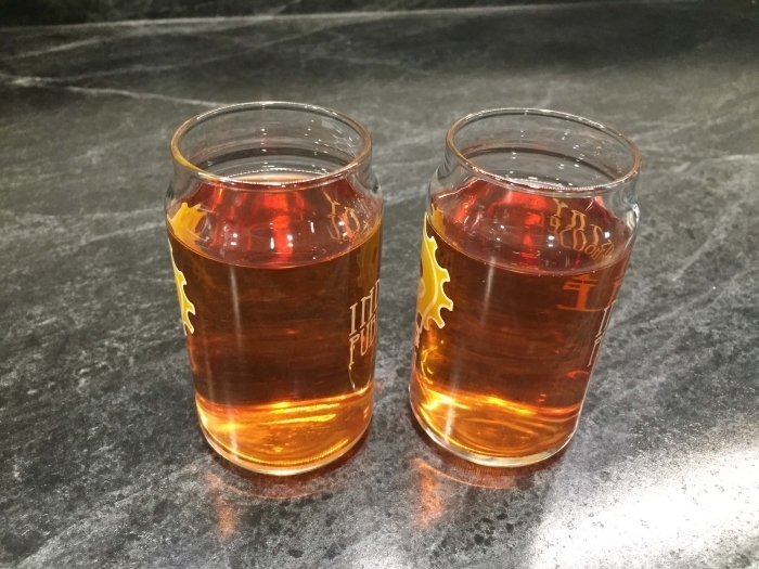 Two small glasses of hard cider on a black countertop