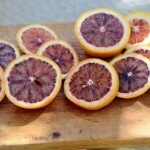 several cut blood oranges on a wooden cutting board